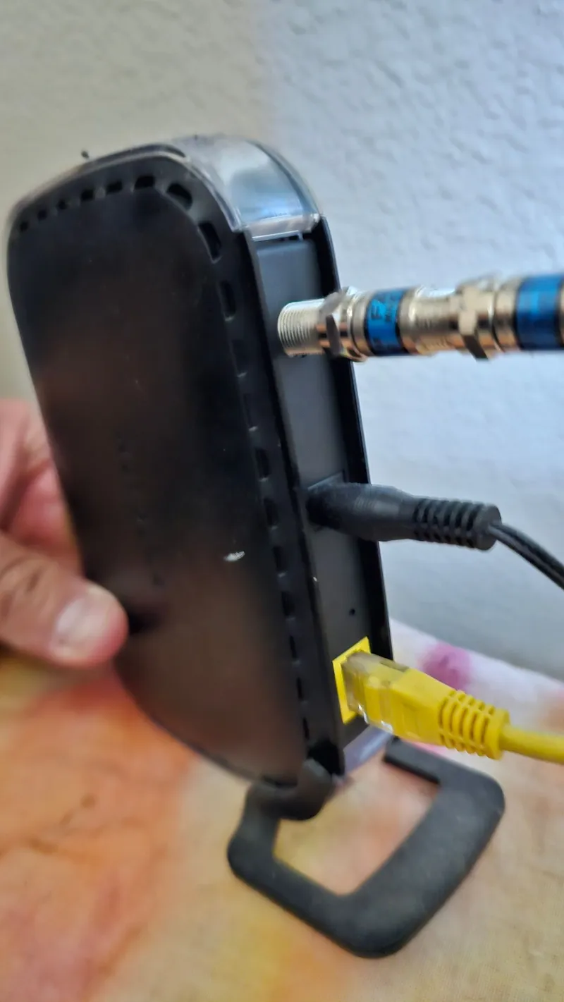 Hands connecting coax and ethernet cables to a cable modem during an internet setup