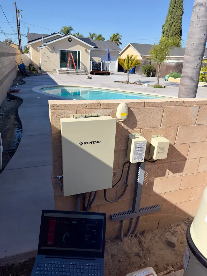 Pool automation control panel installed on a block wall beside a backyard pool